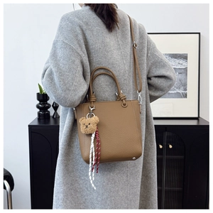 Detail of brown pebbled leather tote bag with teddy bear charm on model in gray coat
