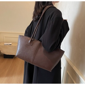 Detail shot of a large brown leather tote bag with long shoulder straps on a model