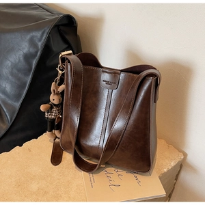 Macro shot of dark brown leather bucket bag with plush rabbit charm and flap closure