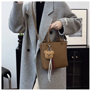 Detailed texture of brown lychee grain leather tote bag with a cute plush bear charm