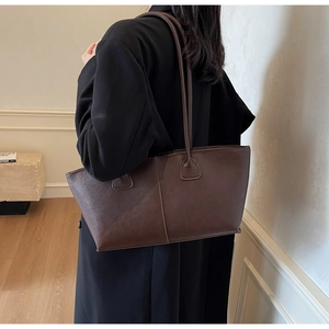 Detail view of large dark brown matte faux leather tote bag worn by a model in interior