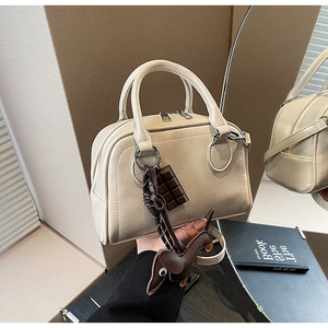 Detailansicht der beigen Boston-Tasche aus Leder mit Gold-Zippern und süßen Anhängern