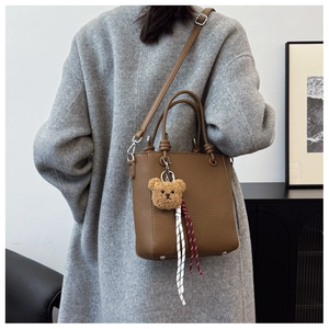 Detail of brown litchi pattern leather tote with cute plush bear and woven rope charm