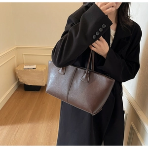 Macro detail of dark brown leather tote bag showing vertical stitching and matte texture