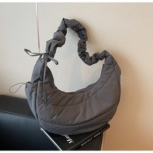 Detail of dark grey quilted half moon bag with ruffled strap and side bow accent