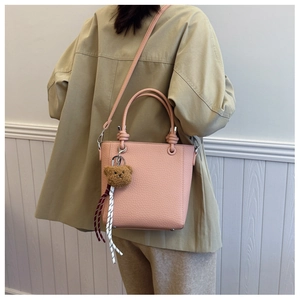 Detail view of pink pebbled tote bag with bear charm shown from a side-back angle