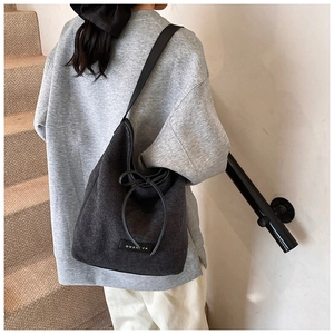 Detail of dark grey tweed bucket bag with black drawstring and OUSHIYA label detail