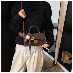 Details einer dunkelbraunen quadratischen Handtasche mit goldenem Drehverschluss und Anhänger
