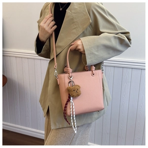Close-up of pink lychee grain leather tote bag with cute plush bear charm and strap