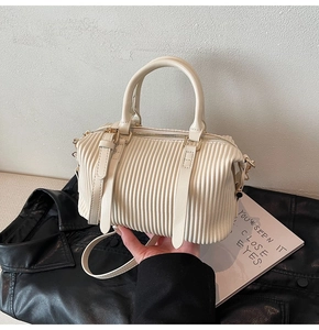 Detail der cremeweißen Boston Bag mit Plissee-Struktur auf schwarzem Ledergrund