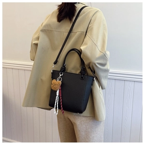 Rear view of model wearing a black pebbled leather bucket bag with a plush bear charm