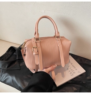 Makro-Detail der pfirsichrosa Plissee-Handtasche mit Wellenstruktur und Goldbeschlägen
