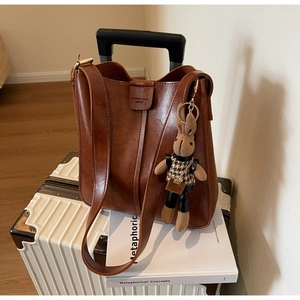Detail of warm brown leather bucket bag with embossed logo and rabbit charm on a suitcase