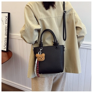 Detail of black pebbled leather tote bag with plush bear charm and adjustable strap