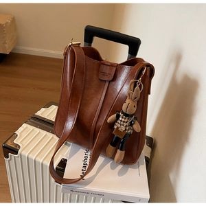 Brown vintage leather bucket bag with a cute knit rabbit charm on a white suitcase