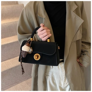 Detail einer schwarzen Handtasche mit goldenem Drehverschluss und Plüsch-Anhänger