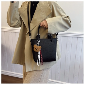 Detail of black lychee grain leather tote bag with knotted handle and plush bear charm