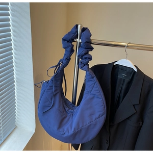 Detail of navy blue quilted puffer crescent bag featuring stylish pleated shoulder strap