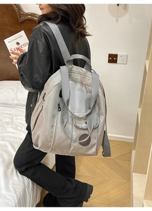 Light grey nylon backpack showing wide straps and side zipper on a female model