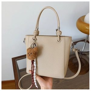 Detail of beige lychee pattern PU leather handbag with knot handle and teddy bear charm
