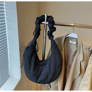 Detail of black quilted puffer crescent bag with wide pleated strap and drawstring accents