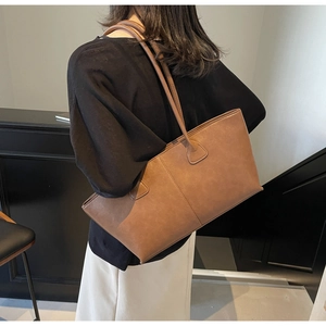 Detailed back view of a large brown leather tote bag worn on the shoulder by a model