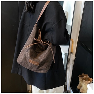 Detail of dark brown herringbone tweed bucket bag with leather drawstring and OUSHEYA logo