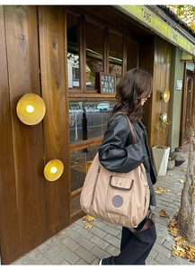 Outdoor shot of a khaki nylon tote bag featuring front flap pockets and a wide strap