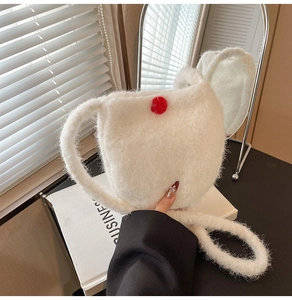 Close-up of white plush bucket bag with soft faux fur texture and red pompom detail