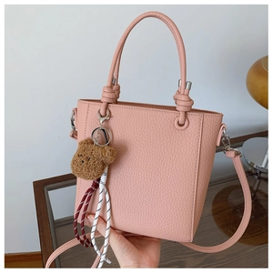 Detailed view of pink pebble grain bucket bag with teddy bear charm and woven tassel