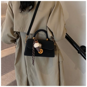 Detailansicht einer schwarzen Handtasche mit goldenen Beschlägen und Plüsch-Anhänger