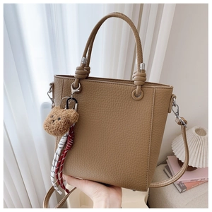 Detailed view of a brown pebbled leather bucket bag with cute bear charm and woven rope