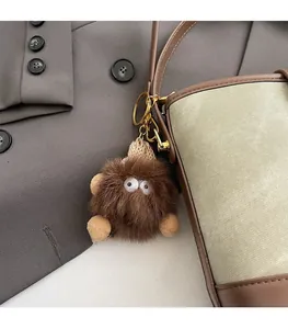 Close-up of a brown plush monster charm on a beige canvas and leather crossbody bag