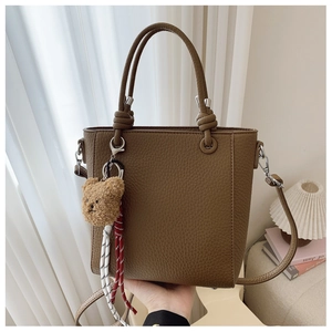Detail view of brown pebbled leather bucket bag with cute bear charm and knotted handle