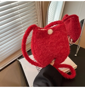 Detail of red plush bucket bag with white pom-pom decoration and fuzzy shoulder strap
