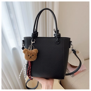 Detail of black pebbled leather tote with knotted handles and a cute bear charm