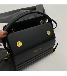 Detail of black textured leather handbag with gold magnetic closures and flap design