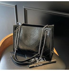Detail of black V-quilted faux leather tote bag with metallic chain strap and soft texture