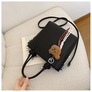 Detail of black pebbled leather bucket bag with knot handle and plush bear charm