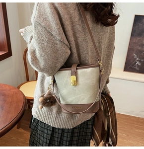 Detail of light green suede bucket bag with gold hardware and plush brown charm on a model