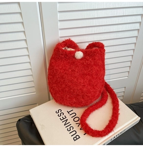 Close-up of red plush bucket bag with soft faux fur texture and white pom-pom detail