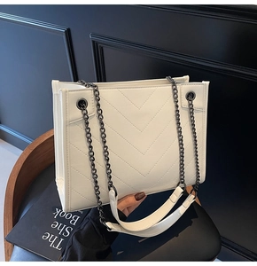 Close-up of white quilted handbag with V-shaped stitching and black chain strap