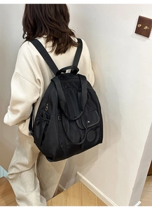 Detail of black nylon backpack featuring side pockets and front flap with snap button