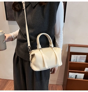 Detail einer cremefarbenen Faltenhandtasche mit goldenen Beschlägen und Gurt am Modell