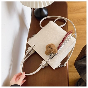 Detail of cream white leather bucket bag featuring a plush bear and woven strap