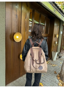 Detailed view of the large tan nylon backpack featuring multi-pocket design on the street