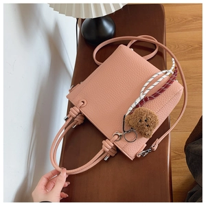 Top view of pink pebbled leather bucket bag with knot handle and bear charm on wood