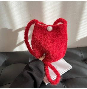 Close-up of vibrant red plush wool bucket bag with white pom-pom detail in a stylish setting