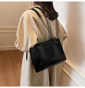 Close-up of black quilted shoulder bag with chain strap worn with a beige coat