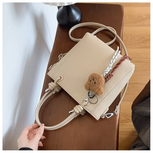 Detail of beige lychee textured leather bucket bag with rope handle and plush bear charm